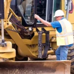Operator climbing into the CAT 140 GC Motor Grader cab using steps and grab rails