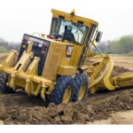 CAT 160K Motor Grader rear ripper and moldboard moving a windrow on a site-preparation job