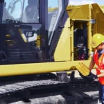 Technician at an open CAT 320 service compartment at ground level