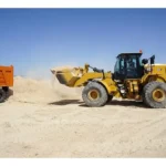 CAT 966 GC Wheel Loader working a sand stockpile next to a dump truck