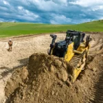 CAT D8 Bulldozer pushing soil on an earthworks site with a site worker nearby